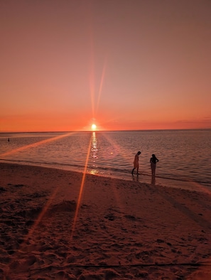 Ein Sonnenuntergang über einem Strand, zwei Personen laufen am Ufer entlang.