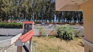 Un balcon donnant sur une zone côtière, un petit bâtiment avec un toit rouge et une route bordée de voitures garées.