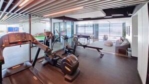 A modern gym with cardio machines, a weight bench, and a seating area with a view of the outdoors. - Belgravia Heights 1 - Tranquil One Bedroom in JVC (Jumeirah Village Circle)