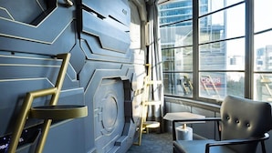 A modern interior with a geometric wall design, a black leather chair, and a view of the city through large windows. - The Capsule Hotel (Sydney)