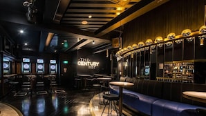 A bar with a modern design, featuring a neon sign, bar stools, and a seating area with a blue couch. - The Capsule Hotel (Sydney)