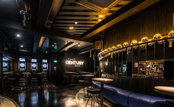 A bar with a modern design, featuring a neon sign, bar stools, and a seating area with a blue couch. - The Capsule Hotel (Sydney)