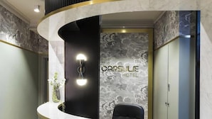 A reception area with a curved counter, a wall-mounted light fixture, and a sign for "The Capsule Hotel". - The Capsule Hotel (Sydney)
