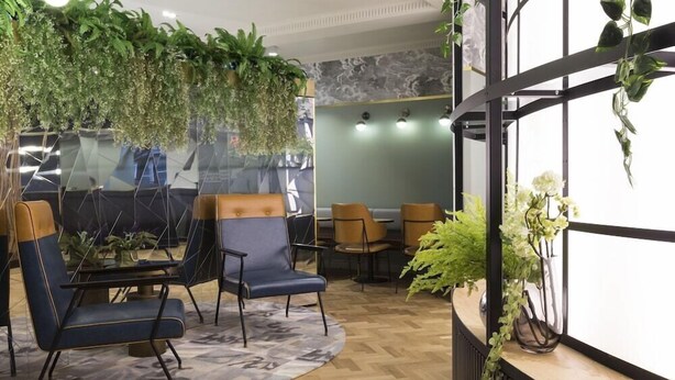 A modern reception area with a curved desk, two blue chairs, and a wooden floor. - The Capsule Hotel (Sydney)