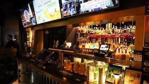 A bar area with a digital menu board, a variety of liquor bottles, and a cash register. - The Capsule Hotel (Sydney)