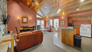 A cozy interior with a wooden ceiling, a kitchen with white appliances, a dining area with a leather sofa, and a stone wall.