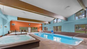 A large indoor swimming pool with a hot tub, lounge chairs, and a view of the outdoors.