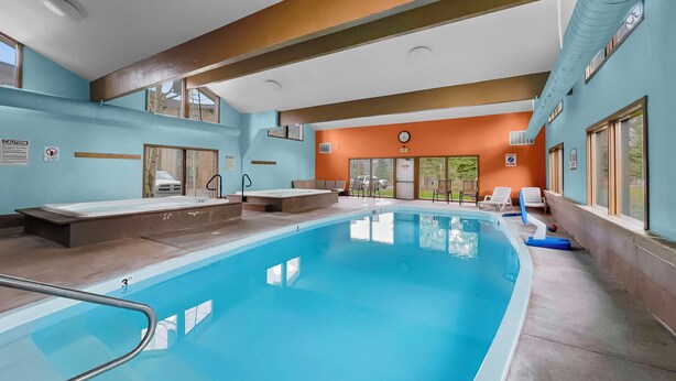 An indoor swimming pool with clear water, a lifeguard chair, and a clock on the wall.