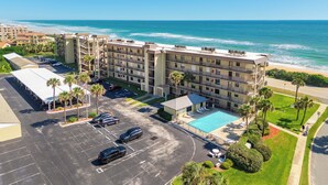 A multi-story hotel with a pool and beach view, parking lot, and a small garden area. - Ormond Beach Oceanfront Accessible | Pool | Seabridge #101 (Ormond Beach)