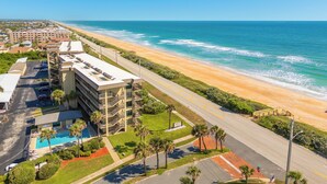 A beachfront hotel with a swimming pool, multiple balconies, and a view of the ocean. - Ormond Beach Oceanfront Accessible | Pool | Seabridge #101 (Ormond Beach)