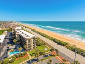 A beachfront hotel with a swimming pool, multiple balconies, and a view of the ocean.
