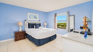 A bedroom with a bed, dresser, and a desk with a model ship. - Ormond Beach Oceanfront Accessible | Pool | Seabridge #101 (Ormond Beach)