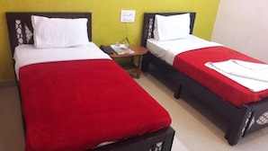 A room with two single beds, each with a red bedspread and white pillows. There is a small wooden table between the beds with a phone and a tray of items. - Maruthi Residency (Bengaluru)