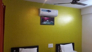 A room with a yellow wall, a ceiling fan, an air conditioner, and two beds with white pillows. - Maruthi Residency (Bengaluru)