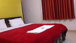 A neatly made bed with a red bedspread, white pillows, and a folded towel on the bed. - Maruthi Residency (Bengaluru)