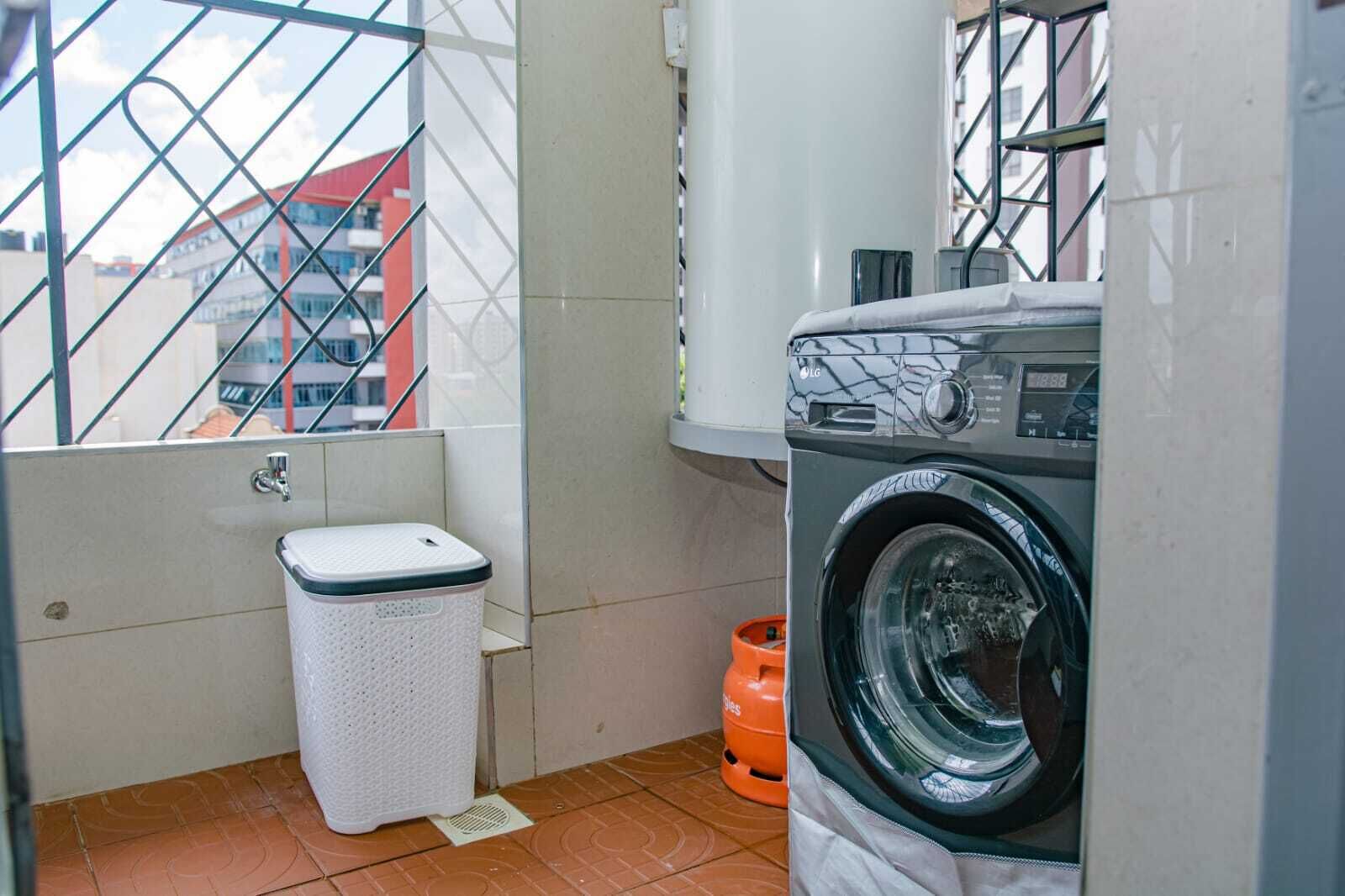 A compact laundry area with a washing machine, a small trash bin, and a water heater.
