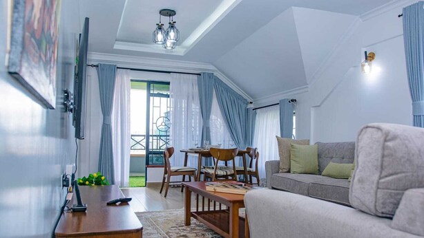 Un salon moderne avec un canapé, une table à manger et des chaises. Un téléviseur est fixé au mur, il y a un luminaire au plafond et une fenêtre avec des rideaux.