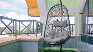 Un balcon avec un fauteuil suspendu, du gazon synthétique et une vue sur les immeubles.