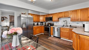 A modern kitchen with wooden cabinets, stainless steel appliances, and a glass dining table with flowers. - Sleeps 12 , Safe area , Close to top attractions (St. Louis)