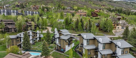 A residential area with modern houses, a swimming pool, and a hilly landscape in the background.