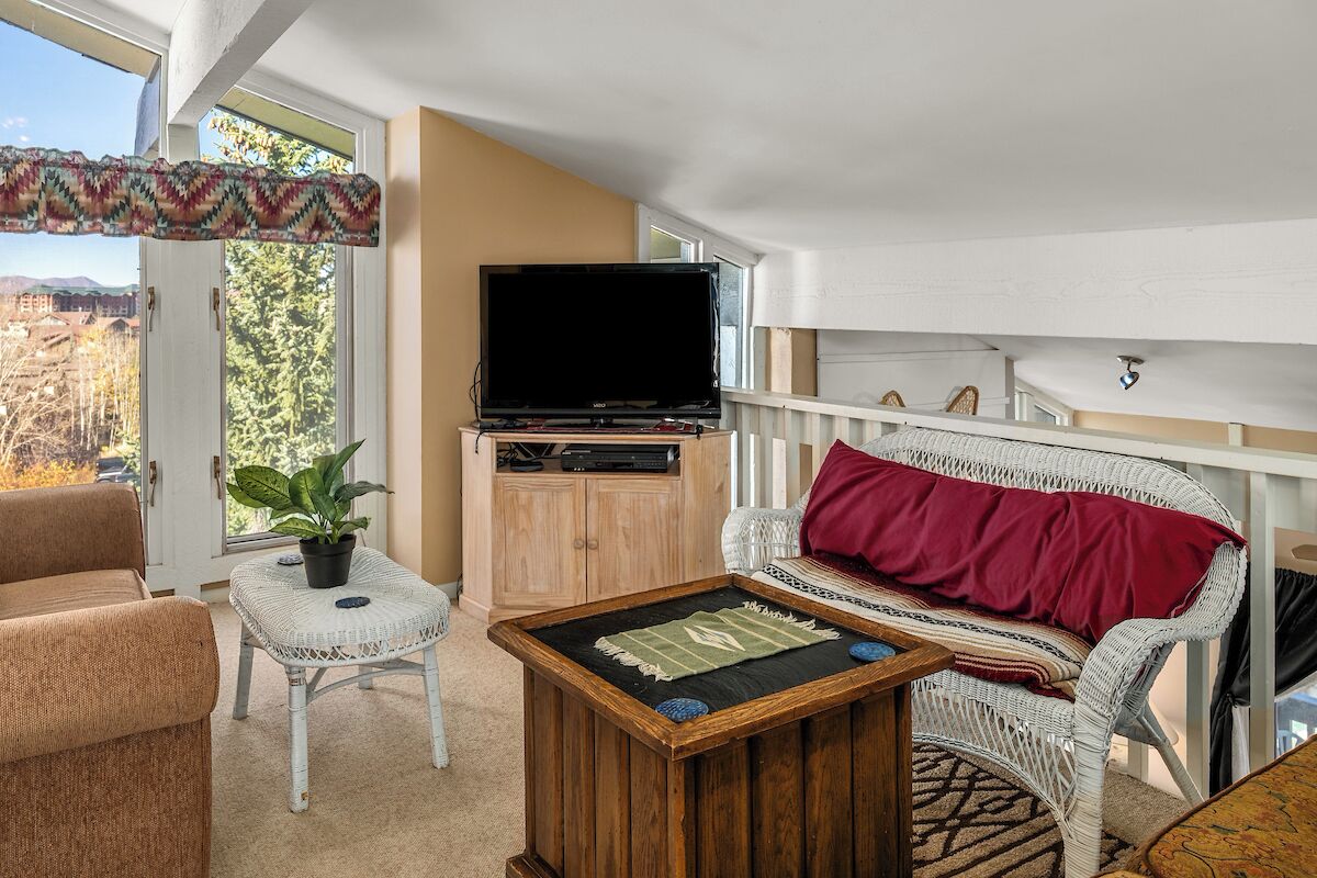 A cozy living room with a television, a sofa, a coffee table, and a potted plant.