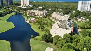 Vista aérea de un complejo turístico con una gran extensión de agua, un campo de golf y varios edificios hoteleros.