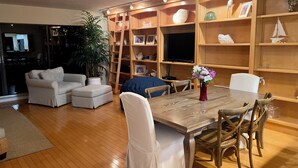Un salón acogedor con una mesa de comedor de madera, sillas blancas, un sofá y un televisor.
