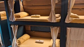 A bunk bed room with curtains, a small table, and a pillow. - Sinhassan Dormitory Hostel (Mumbai)