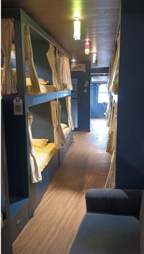 A narrow corridor with bunk beds on either side, wooden flooring, and a small seating area at the end. - Sinhassan Dormitory Hostel (Mumbai)