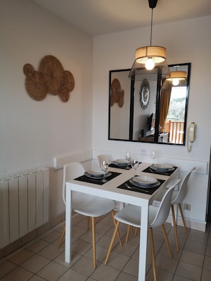 Un comedor con una mesa blanca, cuatro sillas, una lámpara colgante, un espejo grande y un radiador.