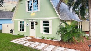 A green house with a white door and windows, a porch with a bench, and a driveway with stepping stones. - Vero Beach Gem: Pool, Game Room, King Beds, minutes to the beaches... (Vero Beach)