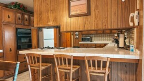 A kitchen with wooden cabinets, a central island with bar stools, a microwave, and a refrigerator. - Rustic Texas Retreat: Ranch style Home Los Ebanitos Ranch  (San Isidro)