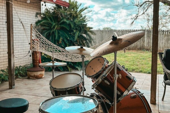 A drum set in an outdoor patio area with a hammock, a brick wall, and a wooden fence in the background.