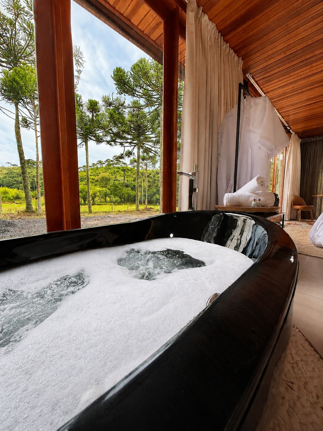 Un jacuzzi con vistas a un paisaje exuberante, vigas de madera y un espacio de descanso acogedor.