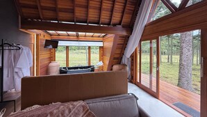 Una cabaña acogedora con una cama grande, un jacuzzi y vistas del bosque circundante.