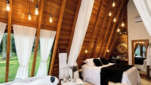 A spacious, high-ceilinged room with a large bed, a sitting area with a chair, a bathtub, and a dining table. - Pousada Maçã Araucária (São Joaquim)