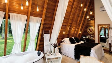 Una habitación amplia con techos altos, una cama grande, un área de descanso con una silla, una bañera y una mesa de comedor.