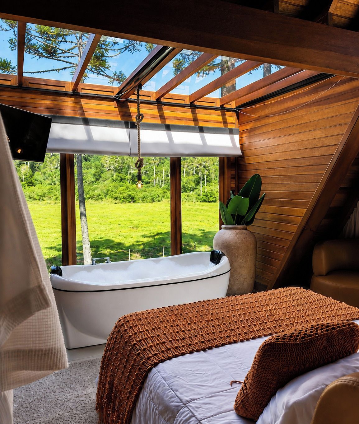 A bedroom with a large window, a bathtub, and a bed with a brown blanket.