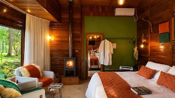 A cozy cabin-style room with a bed, a sofa, a fireplace, and a view of the outdoors.