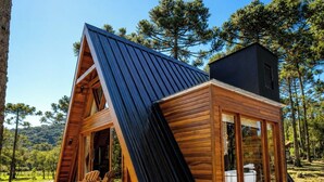 A modern cabin with a sloped roof, large windows, and a wooden deck with chairs. - Pousada Maçã Araucária (São Joaquim)