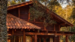 A wooden cabin with a covered porch, a fire pit, and outdoor seating. - Pousada Maçã Araucária (São Joaquim)
