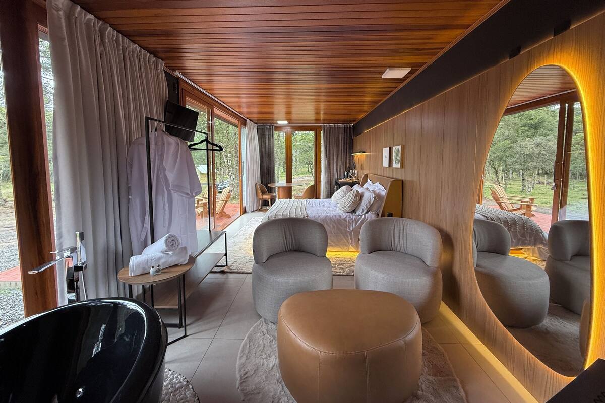 Une chambre moderne avec un grand lit, deux fauteuils, un canapé, une baignoire et un coin repas comprenant une table et des chaises.