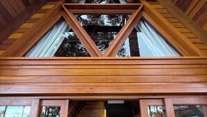 Una cabaña de madera con habitación en el altillo, ventanas amplias y vistas al bosque circundante.