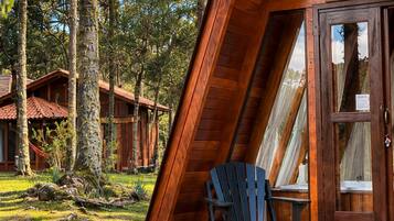 Una cabaña de madera con techo inclinado, una silla Adirondack negra y un brasero en una terraza de madera.