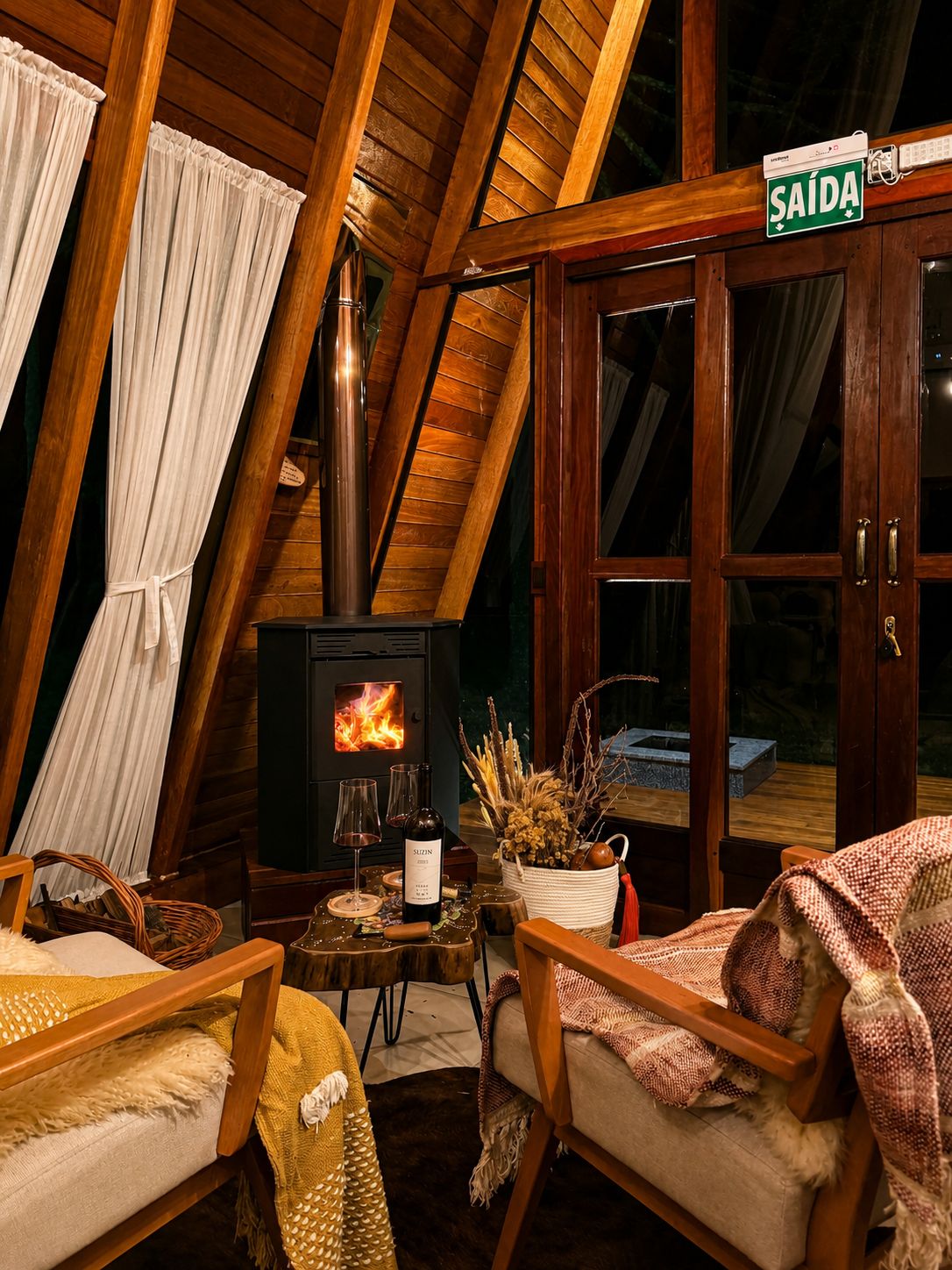 A cozy room with a wood-burning stove, a dining table with wine glasses, and a sign reading 'SAÍDA'.