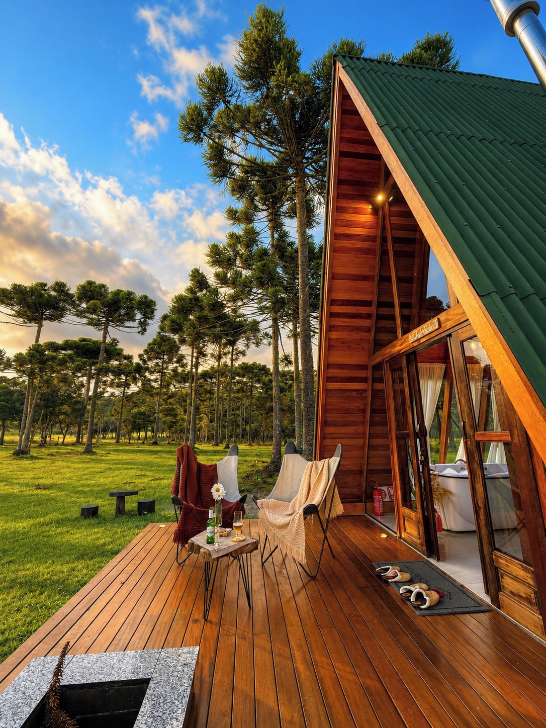 Una terraza de madera con dos sillas, una mesa, un brasero y vistas a un bosque.