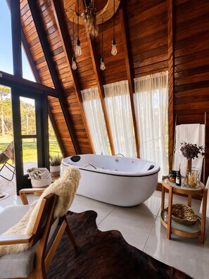 A room with a large bathtub, wooden ceiling beams, and a view of the outdoors. - Pousada Maçã Araucária (São Joaquim)