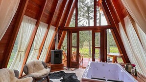 Interior acogedor de una cabaña con techo de madera, un ventanal grande, chimenea, sofá, alfombra de cuero de vaca y un jacuzzi.