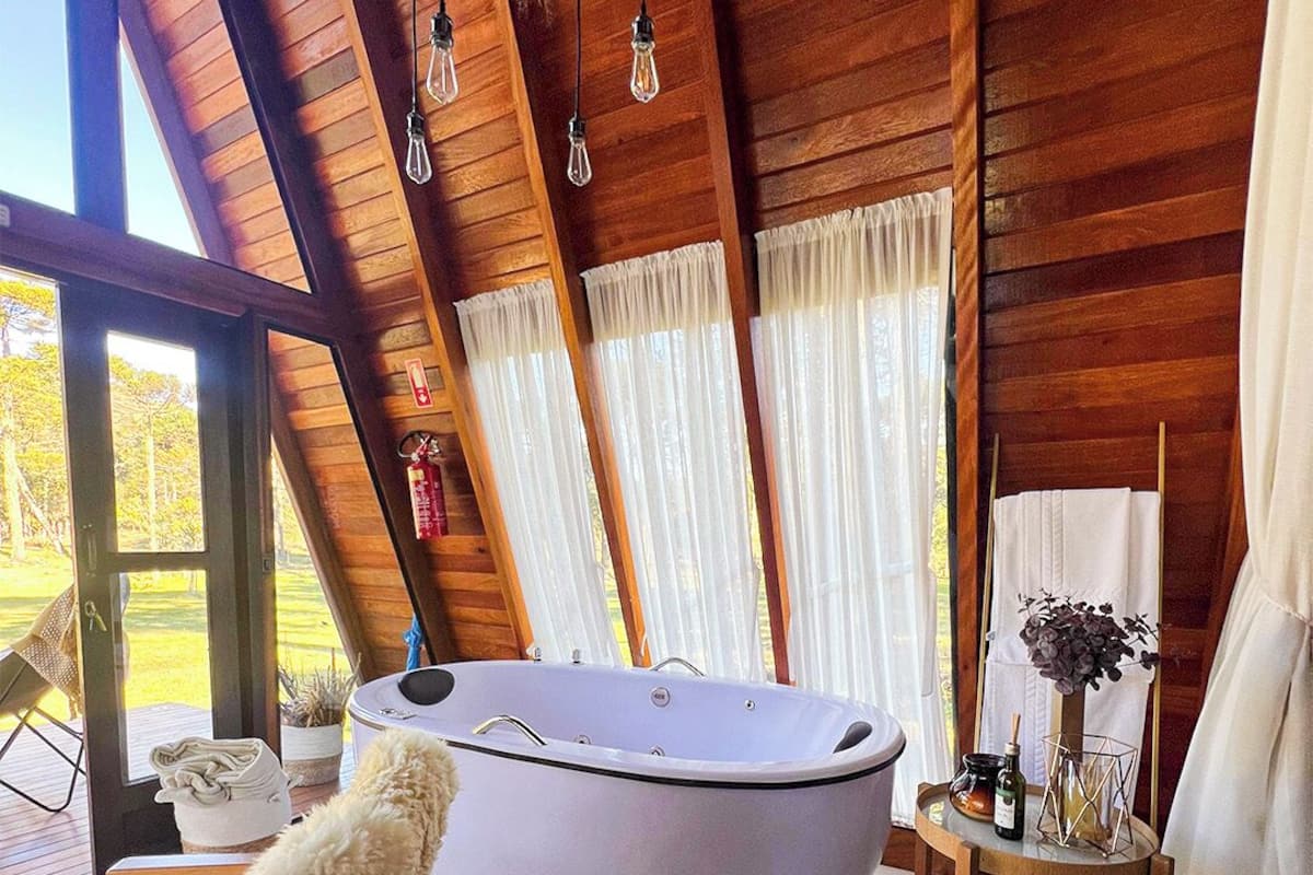 L’intérieur d’un chalet en bois, avec une grande baignoire, une chaise et une petite table sur laquelle se trouvent un vase et une bouteille.