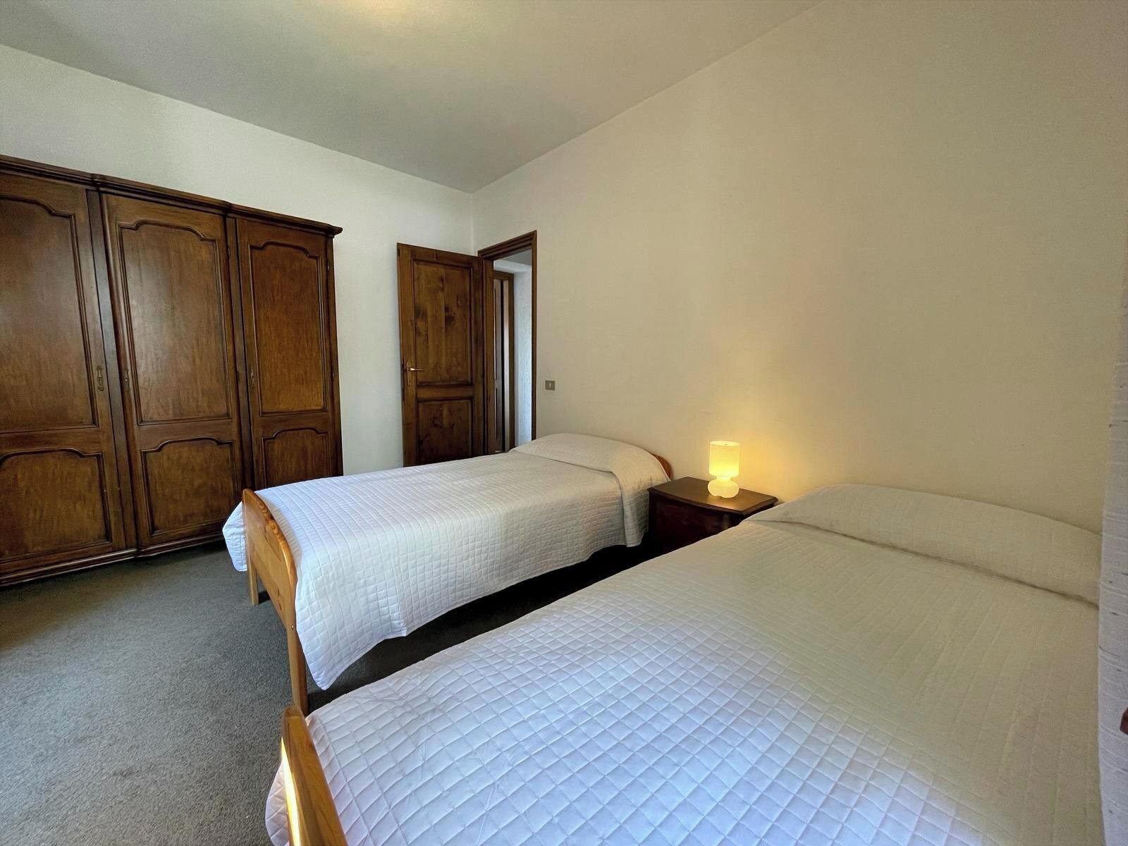 Une chambre avec deux lits simples, une armoire en bois et une table de chevet avec une lampe.
